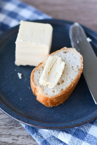 a slice of gluten free bread on a plate with a pat of butter, with more butter beside it, with a butter knife on the other