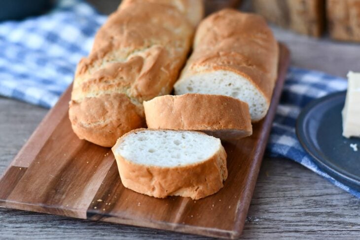 close up view of 2 gluten free French baguettes on a cutting board, with one loaf partially sliced