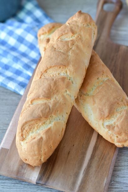 two gluten free french bread loaves, one on top of the other on a wooden cutting board