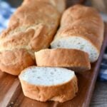 close up view of two vegan baguettes on a wooden cutting board, with one partially sliced